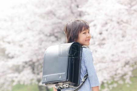 Téléchargez les photos : Mignon garçon japonais enfant avec sac à dos dans le parc de printemps. concept d'éducation - en image libre de droit