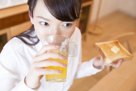 Foto de Chica asiática desayunando con jugo de naranja y tostadas - Imagen libre de derechos