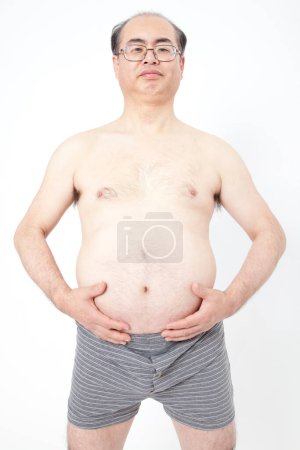 Téléchargez les photos : Japonais gros homme en sous-vêtements montre des dépôts de graisse dans l'abdomen. Concept de mauvaise nutrition, mode de vie sédentaire - en image libre de droit