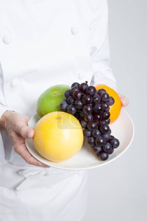 Téléchargez les photos : Photo recadrée du chef masculin tenant des fruits frais sur une assiette blanche - en image libre de droit