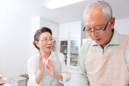 Téléchargez les photos : Senior homme cuisine dans la cuisine avec sa femme - en image libre de droit