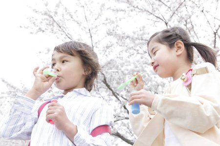 Téléchargez les photos : Heureux écoliers japonais avec bulles de savon dans le parc de printemps - en image libre de droit