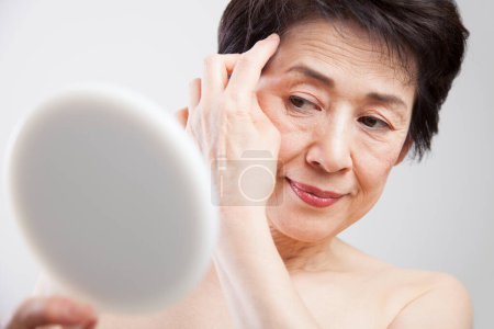 Foto de Retrato de senior asiático mujer aplicación cara crema con espejo - Imagen libre de derechos