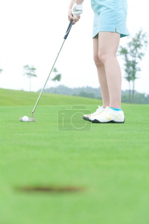 Téléchargez les photos : Jeune golfeuse mettant une balle de golf dans le trou - en image libre de droit