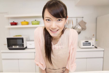 Photo for Beautiful japanese woman wearing apron standing in kitchen - Royalty Free Image