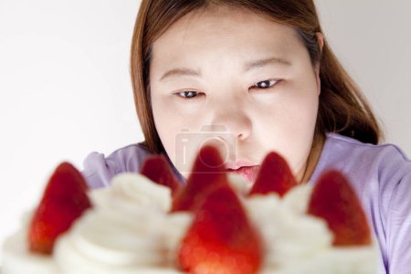 Téléchargez les photos : Portrait studio de femme japonaise en surpoids avec gâteau sur fond blanc - en image libre de droit