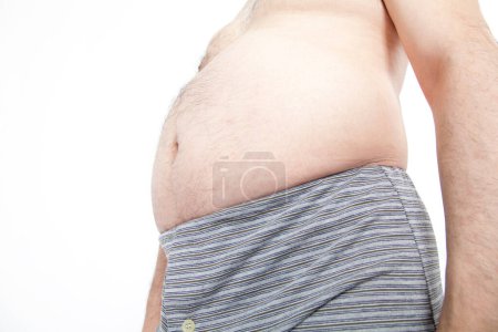 Téléchargez les photos : Gros homme en sous-vêtements montre des dépôts de graisse dans l'abdomen. Concept de mauvaise nutrition, mode de vie sédentaire - en image libre de droit