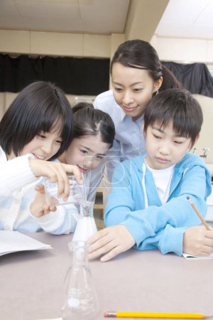 Foto de Niños de primaria japoneses haciendo experimento químico con el maestro en el aula - Imagen libre de derechos