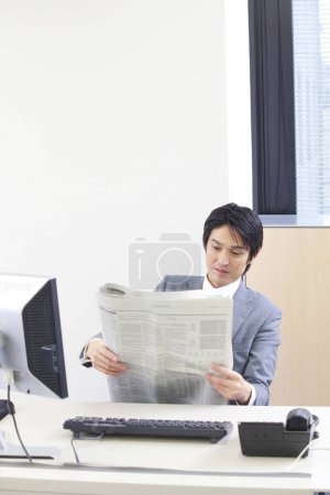 Foto de Un hombre de traje leyendo un periódico en un escritorio - Imagen libre de derechos