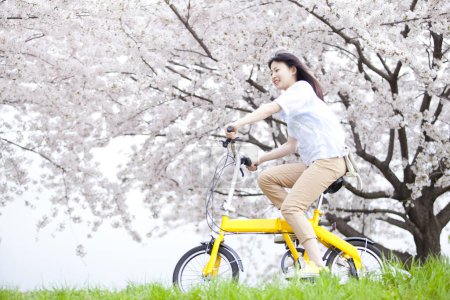 Foto de Feliz japonesa mujer equitación amarillo bicicleta en primavera parque - Imagen libre de derechos