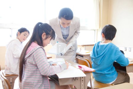 Téléchargez les photos : Enfants japonais assis à des bureaux en classe pendant les cours avec le professeur - en image libre de droit