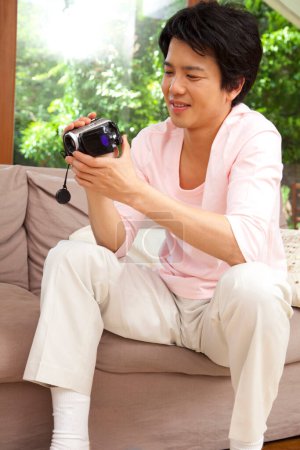 Téléchargez les photos : Portrait asiatique homme à l'aide de caméra vidéo à la maison - en image libre de droit