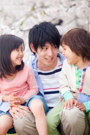 Téléchargez les photos : Happy asian family of three with blooming cherry tree on background - en image libre de droit