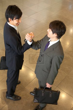 Téléchargez les photos : Deux hommes en costumes serrant la main dans un hall - en image libre de droit
