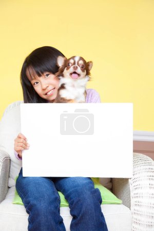 Téléchargez les photos : Souriant fille japonaise avec petit Chihuahua chien tenant papier blanc vierge - en image libre de droit