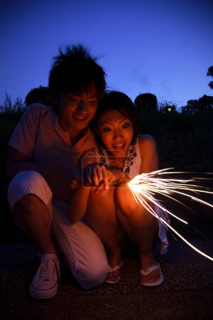 Photo for Happy Japanese man and woman with sparkler in evening - Royalty Free Image