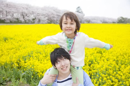 Téléchargez les photos : Jeune père et petit fils s'amusent ensemble à la floraison champ de colza pendant le printemps - en image libre de droit