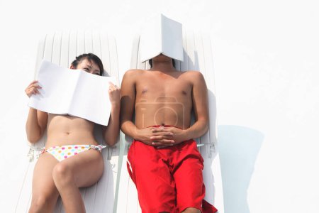 Téléchargez les photos : Jeune couple lisant des livres sur des chaises longues sur une plage - en image libre de droit