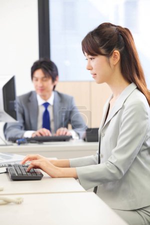 Téléchargez les photos : Une femme assise à un bureau utilisant un ordinateur - en image libre de droit
