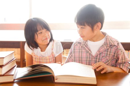 Photo for Cute asian  girl and boy reading book in library - Royalty Free Image