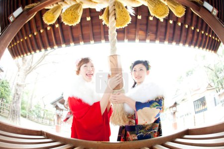 Asiático niñas vestidas en furisode sacudiendo campana en templo después de rezar