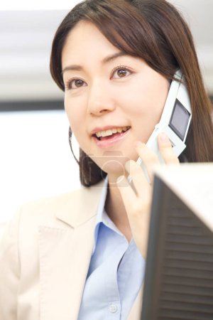 Photo for A woman talking on a cell phone while sitting in front of a computer - Royalty Free Image