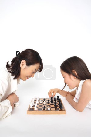 Téléchargez les photos : Souriant japonais mère et fille jouer aux échecs - en image libre de droit
