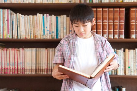 Photo for Japanese boy reading book in school library - Royalty Free Image