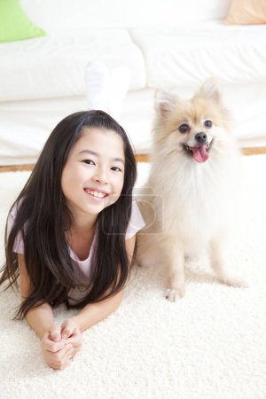Foto de Sonriente chica asiática acostada en el suelo con pomeranian spitz dog - Imagen libre de derechos