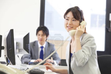 Téléchargez les photos : Une femme parlant au téléphone assise à un bureau - en image libre de droit