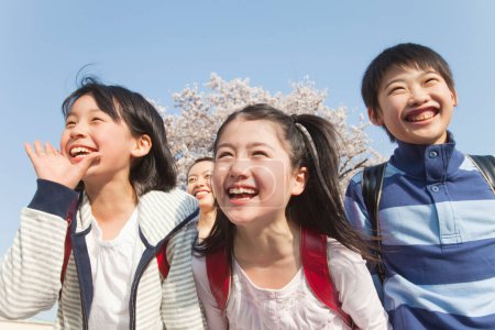 Téléchargez les photos : Enfants japonais souriants avec sacs à dos dans le parc de printemps - en image libre de droit