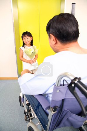 Foto de Lindo poco asiático chica visitando su abuelo en hospital con flores - Imagen libre de derechos