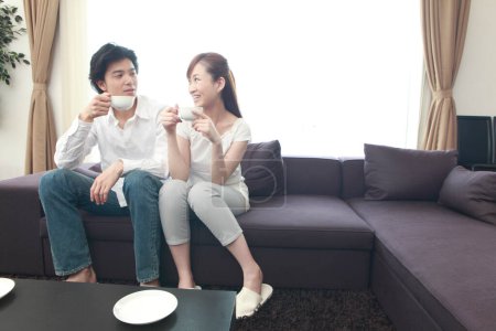 Téléchargez les photos : Un couple assis sur un canapé tenant des tasses à café - en image libre de droit