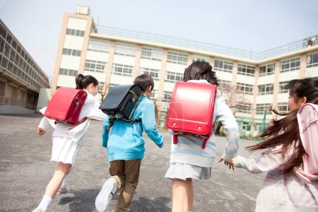 Téléchargez les photos : Groupe d'élèves heureux de l'école primaire en cours d'exécution sur la cour de l'école, vue arrière - en image libre de droit
