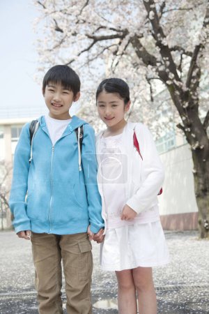 Téléchargez les photos : Jeunes élèves japonais du primaire avec des fleurs de cerisier sur fond - en image libre de droit