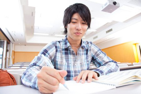 Téléchargez les photos : Asiatique étudiant écriture dans l 'notebook - en image libre de droit