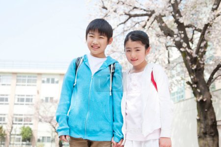 Téléchargez les photos : Jeunes élèves japonais du primaire avec des fleurs de cerisier sur fond - en image libre de droit