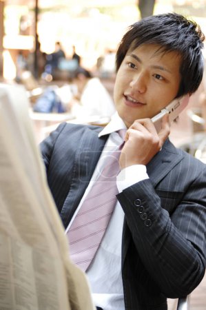 Téléchargez les photos : Homme d'affaires avec téléphone portable lecture journal en plein air - en image libre de droit