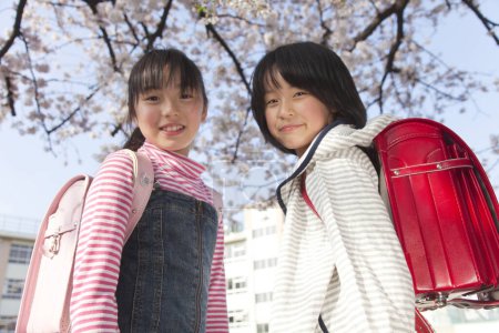 Foto de Sonrientes chicas japonesas con mochilas en el parque de primavera - Imagen libre de derechos
