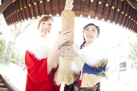 Asiático niñas vestidas en furisode sacudiendo campana en templo después de rezar