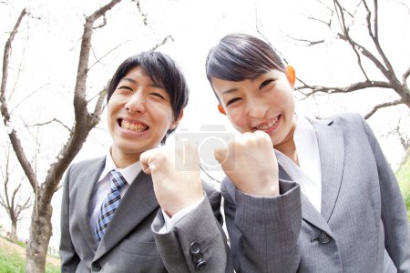 Photo for Portrait of couple of young japanese business partners celebrating success in park during sakura blossoming seasone - Royalty Free Image