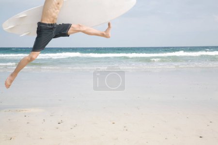 Téléchargez les photos : Photo recadrée de l'homme avec planche de surf sautant sur la plage - en image libre de droit