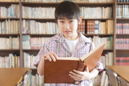 Téléchargez les photos : Japonais garçon lecture livre dans école bibliothèque - en image libre de droit