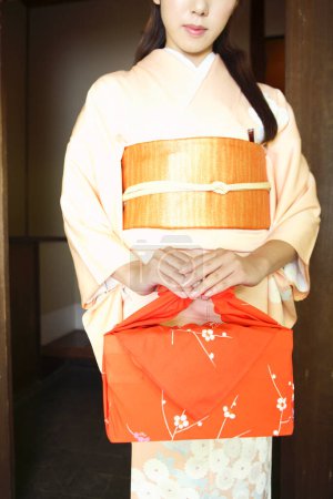 Foto de Retrato de una joven japonesa en kimono tradicional sosteniendo bento envuelto - Imagen libre de derechos