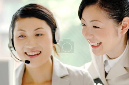 Foto de Sonriente asiático mujer servicio al cliente agente con auriculares y su colega - Imagen libre de derechos