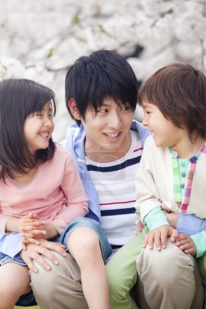 Photo for Happy asian family of three with blooming cherry tree on background - Royalty Free Image