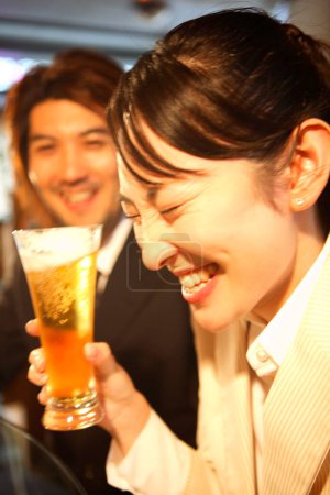Photo for Young japanese office workers in suits drinking beer in bar - Royalty Free Image