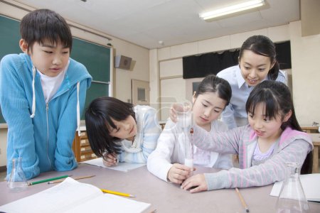 Foto de Niños de primaria japoneses haciendo experimento químico con el maestro en el aula - Imagen libre de derechos