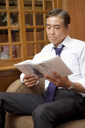 Photo for Mature businessman reading book in room - Royalty Free Image