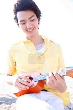 Téléchargez les photos : Asiatique homme jouer ukulele sur mer rivage - en image libre de droit